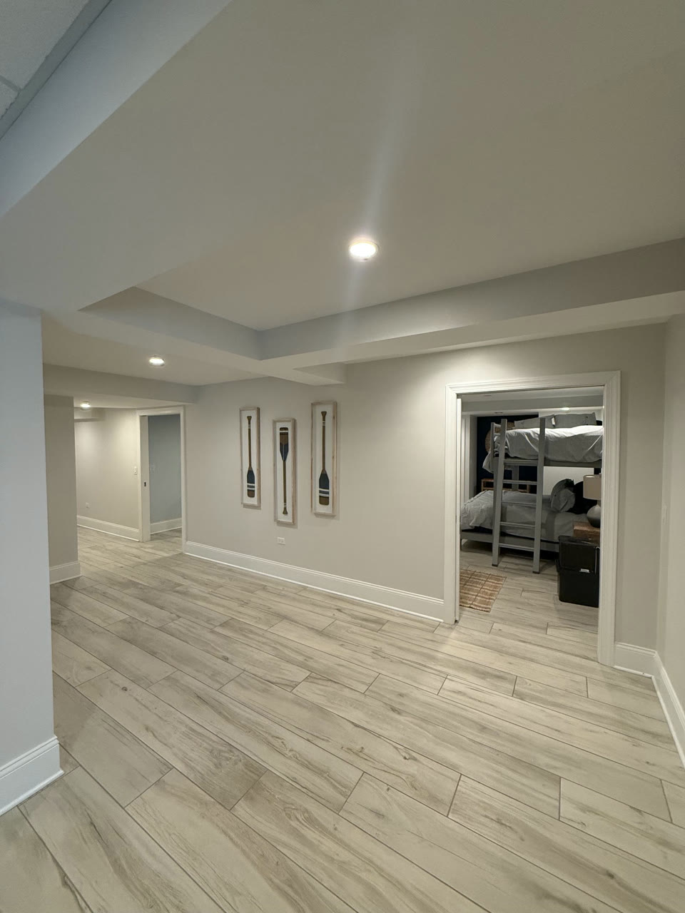 Finished basement hallway with recessed lights, a tray ceiling detail and wood look tile leading to a bunk room